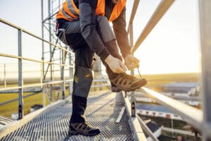 An Industry Worker Tying Shoelace On Work Shoes While Standing O